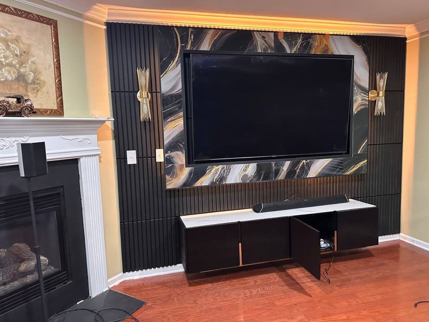 Black fluted panels framing a dramatic black and gold marble field, with warm cove lighting above and a fluted base cabinet