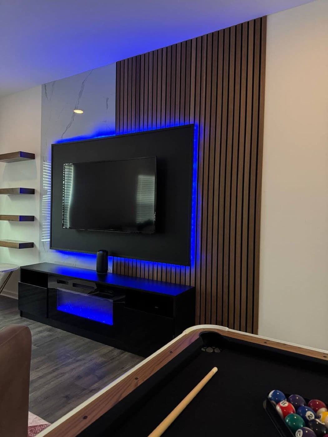 Floor-to-ceiling vertical wood slat wall beside a marble panel, with a backlit TV and floating console