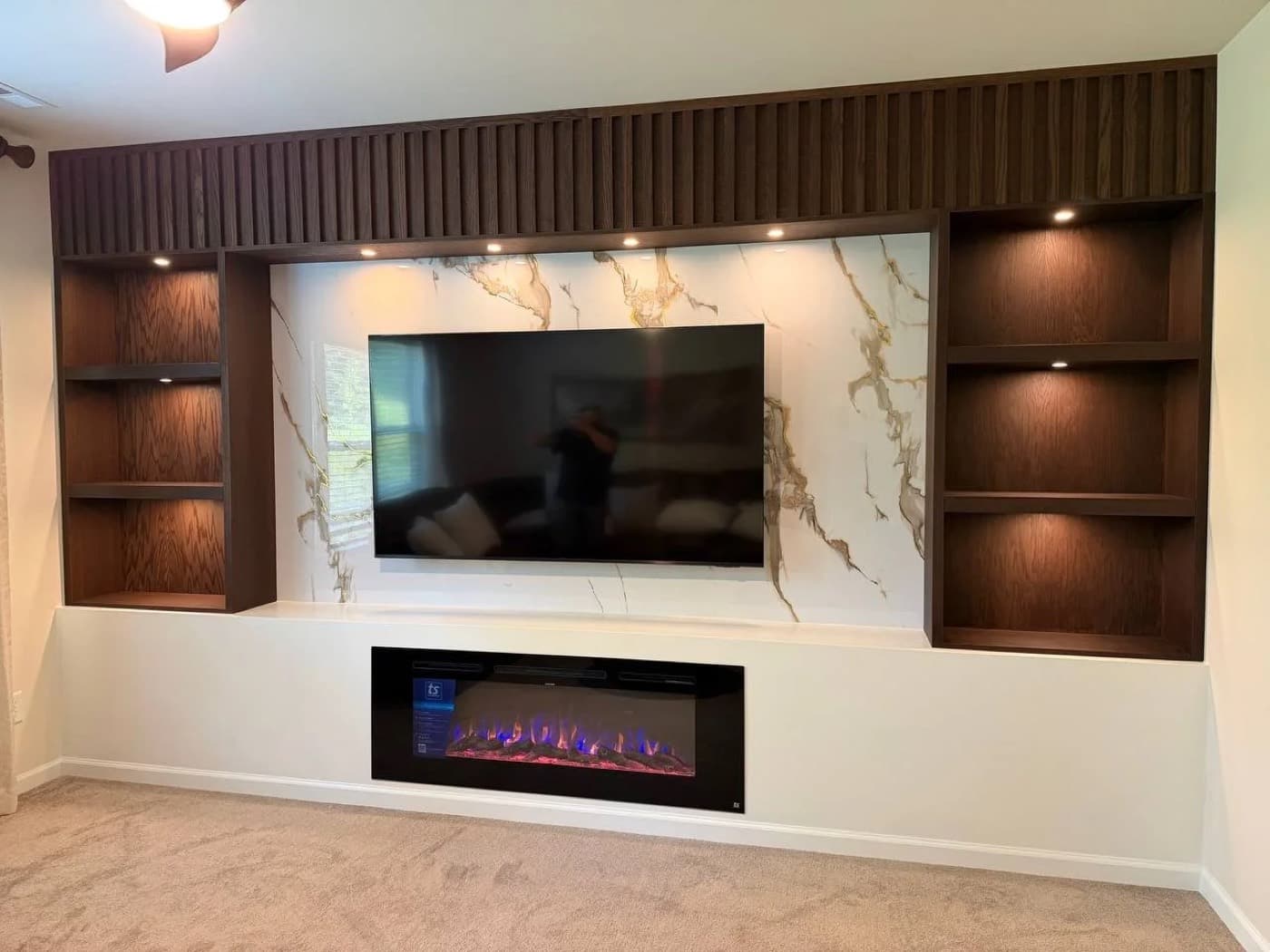 The same custom media wall as built, with the fluted walnut header, marble surround, lit niches and linear electric fireplace installed
